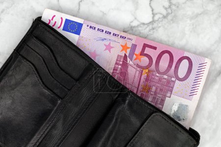 500 euro banknote in a black leather wallet on white marble background, top view of a purse filled with cash