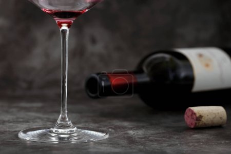 Photo for Empty glass of wine in front of lying wine bottle with cork on dark gray background, concept of alcoholism or excessive alcohol consumption, close-up of last sip of wine. - Royalty Free Image