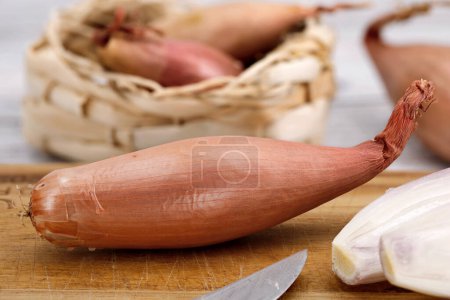 Close-up of a banana shallot on a wooden cutting board with a knife, onion cutting concept.