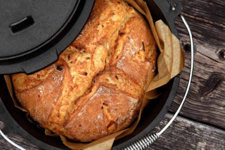 Homemade onion bread baked in a traditional Dutch oven on a rustic wooden background, top view of a freshly baked loaf in a black cast iron pot with a lid.