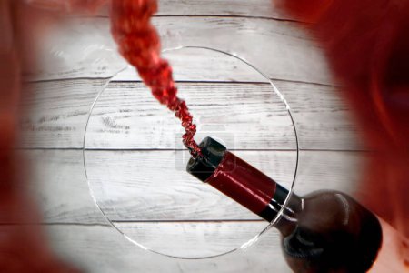 Ein Weinglas wird aus einer Weinflasche mit Rotwein gefüllt, ungewöhnliche Perspektive aus dem Inneren des Glases, das nach oben zur gießenden Weinflasche blickt.