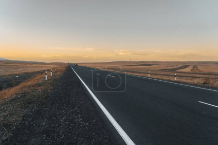 Téléchargez les photos : Route asphaltée à travers les champs au coucher du soleil - en image libre de droit