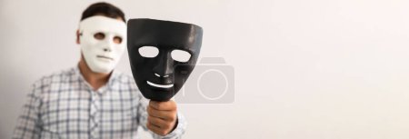 homme portant un masque blanc tenant des masques noirs dans sa main. Masquage social anonyme