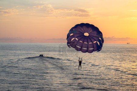 Szene eines Mannes beim Fallschirmspringen mit einem lila Fallschirm über dem Meer