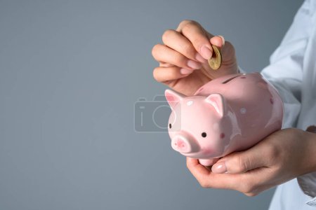 Eine Frau legt einen Groschen in ein Sparschwein, Atelierhintergrund