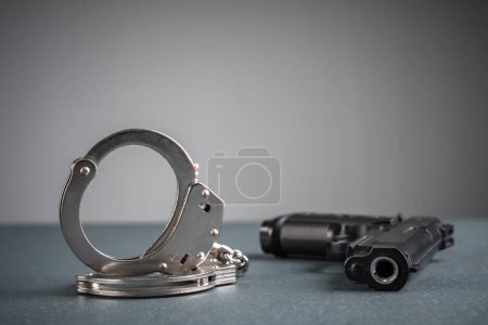 Pistole und Handschellen auf grauem Hintergrund, Archivbild, kriminelles Konzept