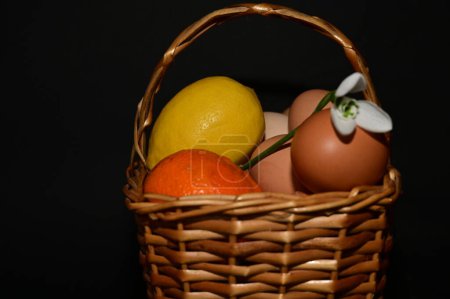 Foto de Easter holiday, eggs, fruits and snowdrop   in  basket on black background - Imagen libre de derechos