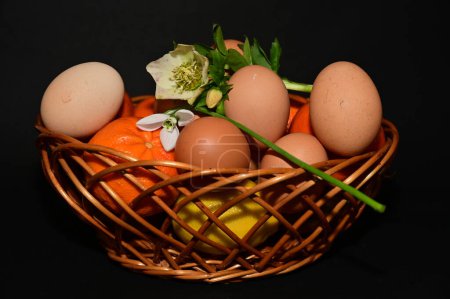 Téléchargez les photos : Easter holiday, eggs, fruits   and flowers in  basket on black background - en image libre de droit
