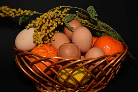 Foto de Easter holiday, eggs, fruits   and flowers in  basket on black background - Imagen libre de derechos