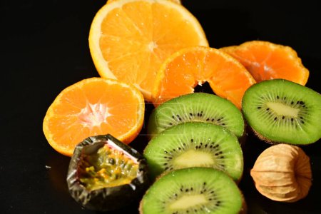 Foto de Kiwi, naranjas, fruta de la pasión fruta fresca madura sobre un fondo negro - Imagen libre de derechos