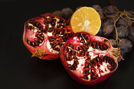 Téléchargez les photos : Grenade fraîche mûre avec raisins et citron sur fond sombre - en image libre de droit