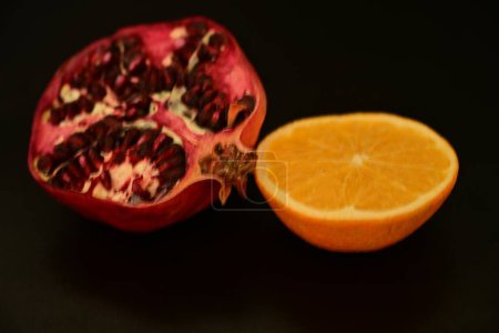 Foto de Fruta de granada con semillas y naranja a la mitad sobre un fondo oscuro. - Imagen libre de derechos
