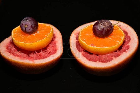Téléchargez les photos : Pamplemousse rouge frais avec des tranches d'orange et des raisins sur fond sombre - en image libre de droit