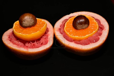 Téléchargez les photos : Pamplemousse rouge frais avec tranches d'orange et châtaignes sur fond sombre - en image libre de droit