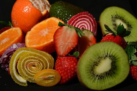 Foto de Surtido de frutas y verduras con gelatinas enrolladas sobre un fondo negro - Imagen libre de derechos