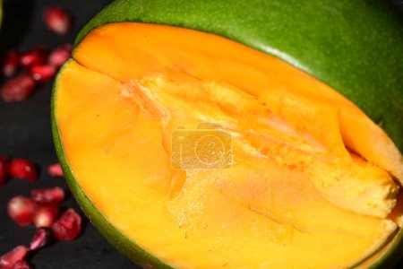 Téléchargez les photos : Fruits de mangue coupés avec des graines de grenade sur fond sombre - en image libre de droit