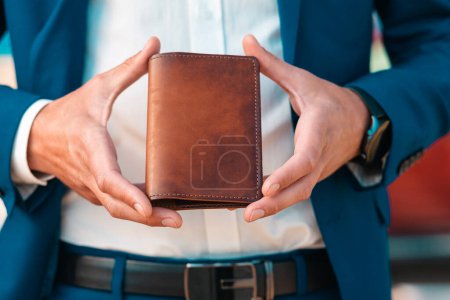 Photo for A businessman in an elegant blue jacket and white shirt shows off a leather brown cover for passport. Close-up of the hands. The concept of style and fashion. - Royalty Free Image