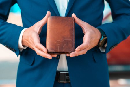 Photo for A businessman in an elegant blue suit shows off a brown handmade leather document holder. Close-up of the hands. The concept of style and fashion. - Royalty Free Image