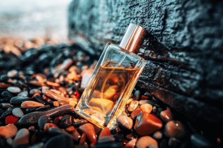 Photo for Transparent rectangular glass bottle of golden perfume on a wet pebbles, near a large stone. Cosmetics and perfumes. - Royalty Free Image