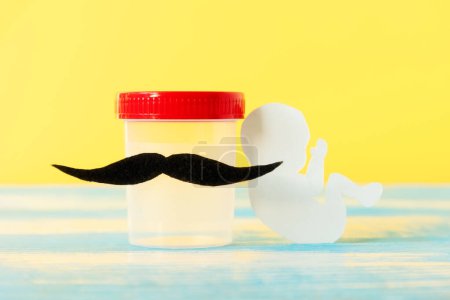Foto de Test-tube with sample of sperm with felt moustache and paper embryo. Yellow background. Concept of artificial insemination and urology. - Imagen libre de derechos