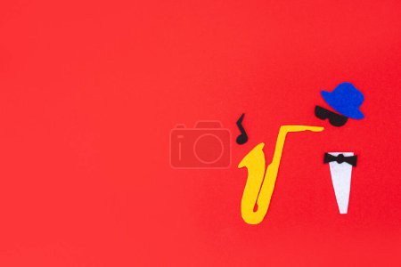 Photo for Jazz Day. Silhouette of a musician with a saxophone from which melodies flew out, on a red background, cutted out of felt. Flat lay. Copy space. - Royalty Free Image