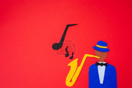 Photo for International Jazz Day. Silhouette of a musician with a saxophone from which melodies flew out, on a red background, cutted out of felt. Flat lay. Copy space. - Royalty Free Image