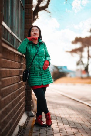 Téléchargez les photos : A fashionably dressed elderly beautiful Caucasian woman in a green jacket posing at the street. Active recreation of retired people. - en image libre de droit