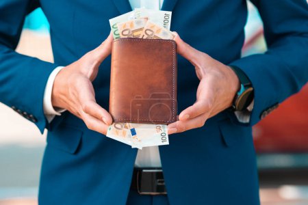 Photo for Rich businessman in a blue jacket shows off a leather brown wallet full of euro cash. Close-up of the hands. The concept of banking and wealth. - Royalty Free Image