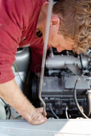 Photo for The concept of disability of people and their adaptation to life. A disabled man repairs a car. There are no fingers on his hands. Disabled from childhood. Vertical. - Royalty Free Image