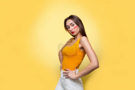 Feminism, girl power, and the concept of equal rights and independence for women. Caucasian young woman with makeup in an orange t-shirt posing in profile. Yellow background. Isolate. Copy space.