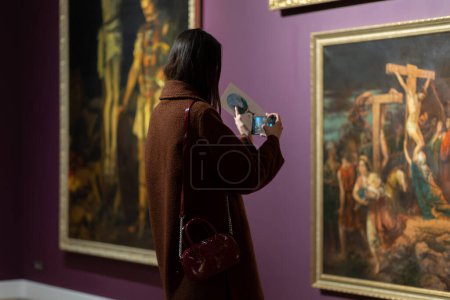 Téléchargez les photos : Vue arrière de la femme prend une photo du chef-d'œuvre en exposition. Concept de Journée des musées. - en image libre de droit