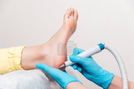 Photo for Podologist does hardware peeling of the skin of the heel. Close-up of smooth foot and master's arms. The concept of professional pedicure and chiropody. - Royalty Free Image