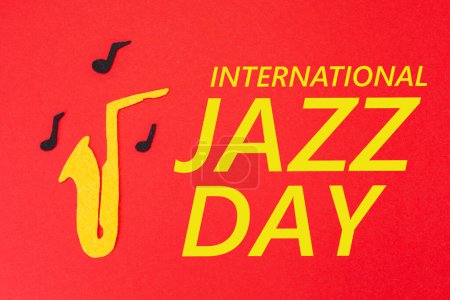 Photo for International Jazz Day. Silhouette of a saxophone from which melodies flew out, on a red background, cutted out of felt. Flat lay. - Royalty Free Image