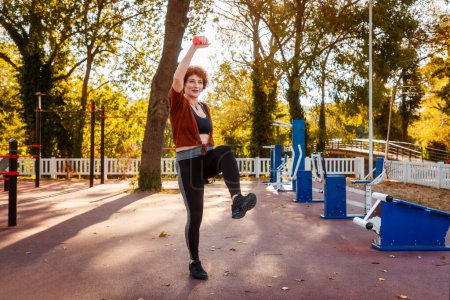 Photo for Fitness and aerobic at city park. Mid adult Caucasian ginger hair woman is doing sports. Concept of healthy lifestyle. - Royalty Free Image