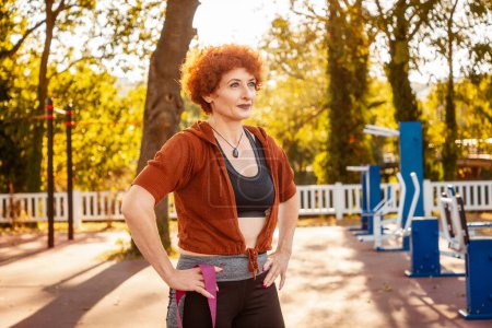 Photo for Adult Caucasian woman with makeup and ginger curly hair posing in sports park. Relax after training. Concept of healthy lifestyle. - Royalty Free Image