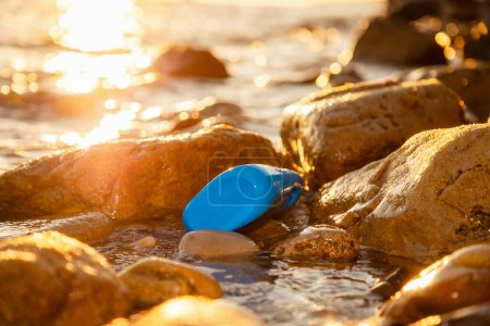 Photo for Close-up of blue plastic bottle lying in coastal rocks of sea. Sunset illuminates shore. Concept of environmental pollution. - Royalty Free Image