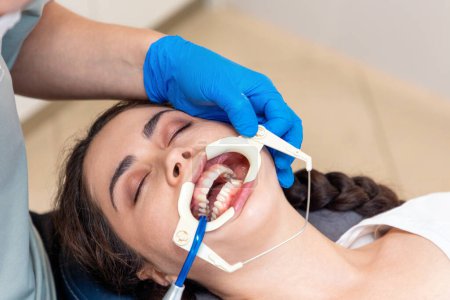 Close-up top view of young Caucasian woman lying at reception in dental office. Dentist puts retractor on woman. Concept of dentistry and orthodontics.