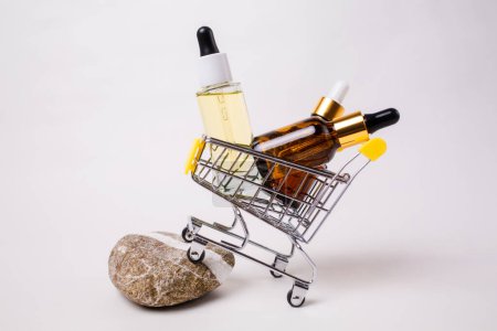 Photo for Mini shopping cart filled with cosmetics bottles, standing on a decorative stone. White background. The concept of shopping cosmetics. - Royalty Free Image