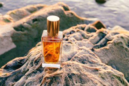 Photo for Top view of rectangular glass bottle with golden perfume at rocks. Fragrance marketing. - Royalty Free Image