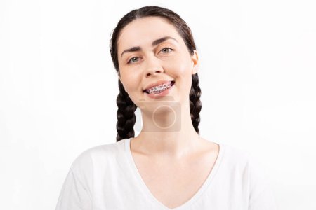 Photo for Portrait of smiling Caucasian young woman with ligature braces on her teeth. White background. Concept of orthodontic treatment and dentistry. - Royalty Free Image