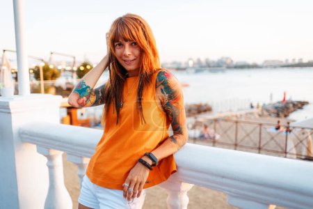 Photo for Portrait of young smiling beautiful Caucasian woman with tattoos leaning on balustrade looking at camera. Concept of freedom and psychology. - Royalty Free Image