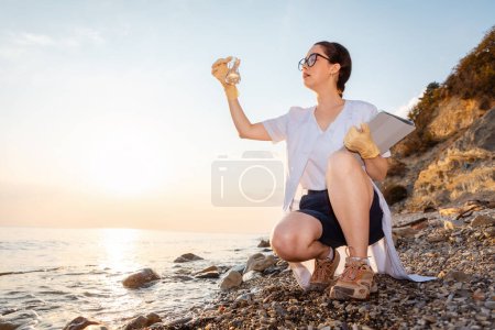 Photo for Bottom view of young Caucasian woman ecologist in rubber gloves looking at test flask of water. Copy space. Concept of ecology and recycle resources. - Royalty Free Image