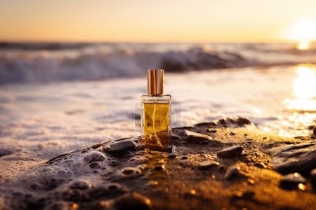 Photo for Rectangular glass bottle with golden perfume washed by sea surf, consecrated by setting sun. Natural perfumes and cosmetics. - Royalty Free Image