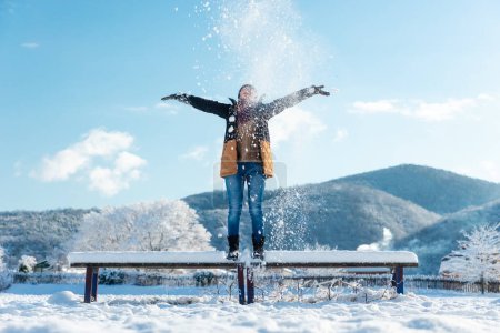 Photo for A happy young woman is standing on a bench with snow thrown on top. Winter Christmas holidays. - Royalty Free Image