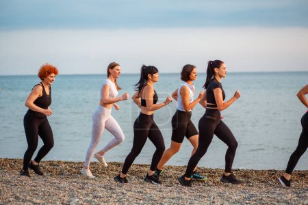 Photo for Side view of group of adult Caucasian women jogging in row at beach. Sea in horizon. Concept of healthy lifestyle and wellness. - Royalty Free Image