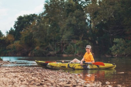 Welttourismustag. Eine junge, glückliche Frau sitzt entspannt in einem gelben Kajak am Ufer des Flusses. Das Konzept des Kajakfahrens und der Outdoor-Aktivitäten.