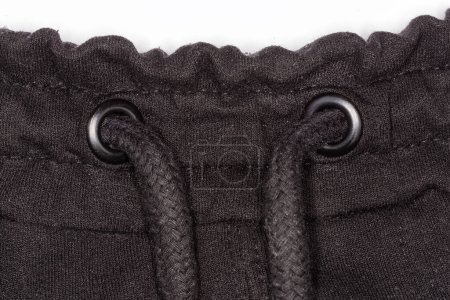 Photo for Fragment of the black knitted pants waist with drawstring inserted through the holes reinforce with eyelets, close-up - Royalty Free Image