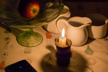 Téléchargez les photos : Bougie brûlante dans le petit chandelier sur la table à manger recouvert de toile huilée parmi les différentes vaisselle lors d'une panne d'électricité - en image libre de droit