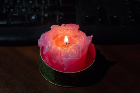 Brennende dicke kurze rote Kerze auf dem Tisch gegen die Tastatur während eines Stromausfalls