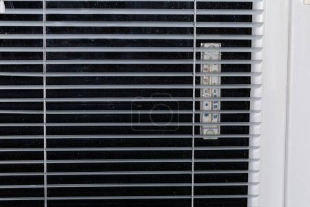 Foto de Parte de la ventana moderna con cristal de ventana cubierto con gotas de agua y termómetro exterior adjunto, vista interior a través de las persianas iluminadas desde el interior por la noche - Imagen libre de derechos